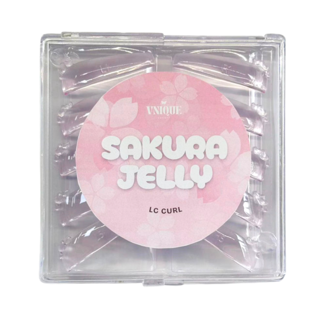 A square clear plastic package containing multiple translucent pink hair extensions, with a large round pink label reading 'SAKURA JELLY' and smaller text 'UNIQUE' and 'lc curl'.