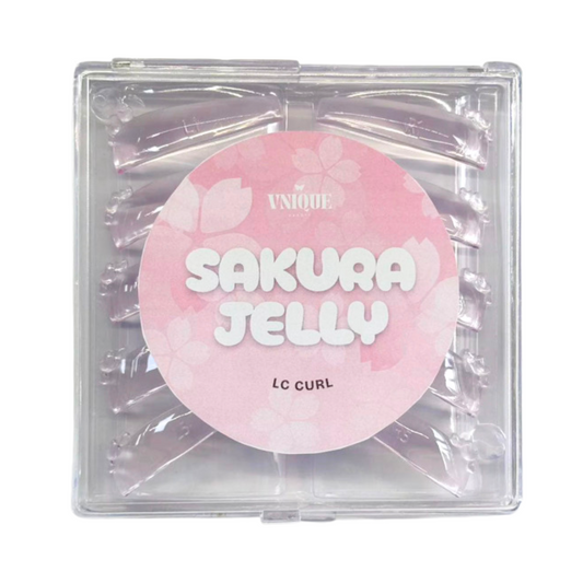 A square clear plastic package containing multiple translucent pink hair extensions, with a large round pink label reading 'SAKURA JELLY' and smaller text 'UNIQUE' and 'lc curl'.