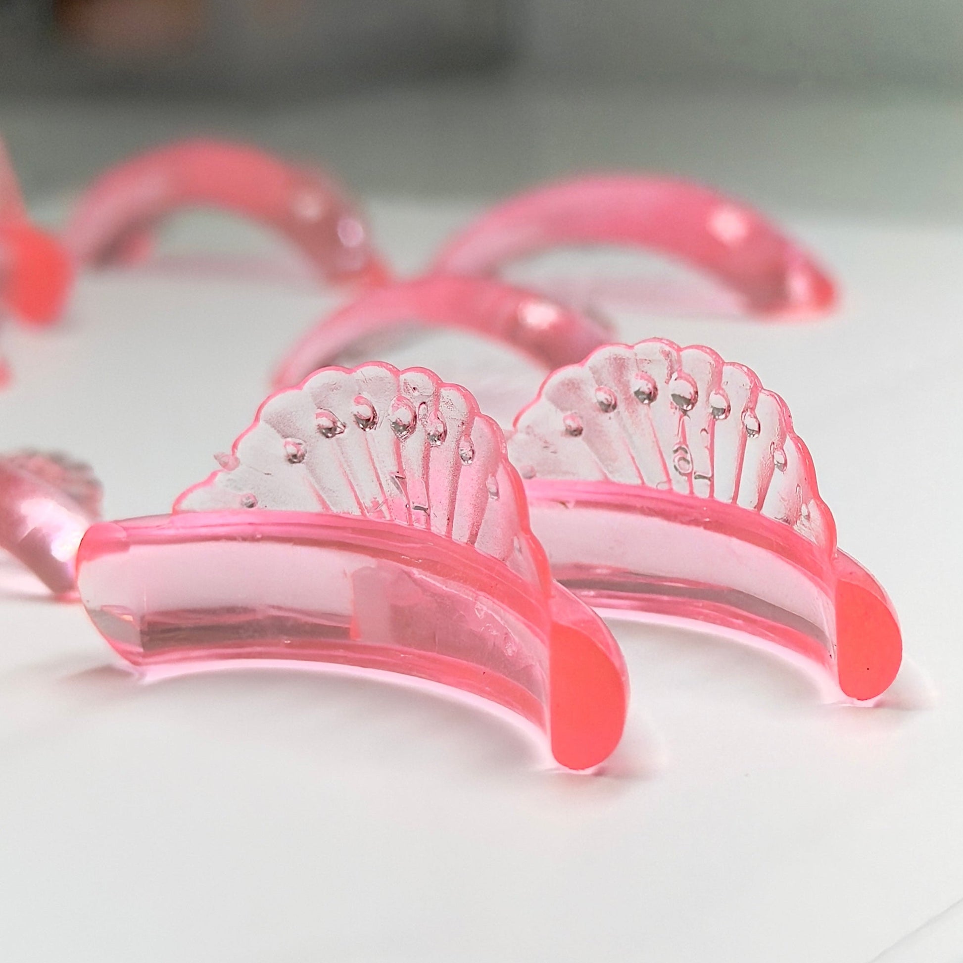 A close-up of several translucent pink curved hair extensions or clip-in hair pieces arranged on a white surface, with shallow depth of field focusing on the front pieces.