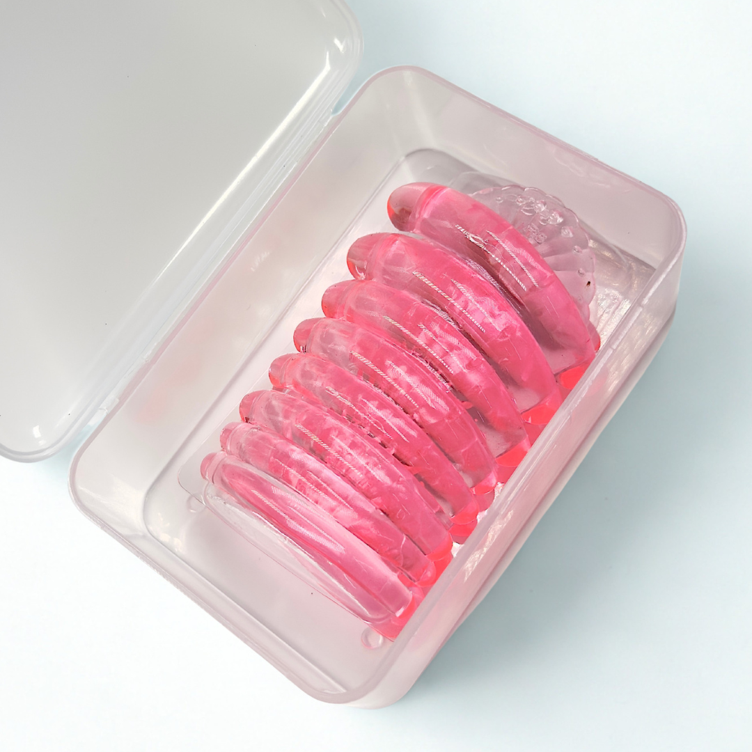 A set of pink translucent silicone or plastic hair clips arranged inside an open translucent pink storage container on a clean white background.